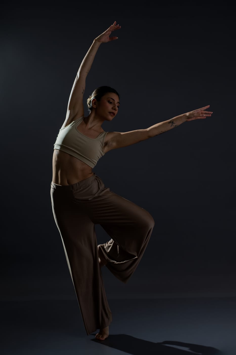 Bailarina em pose de dança contemporânea, com luz de estúdio recortando o corpo no fundo escuro