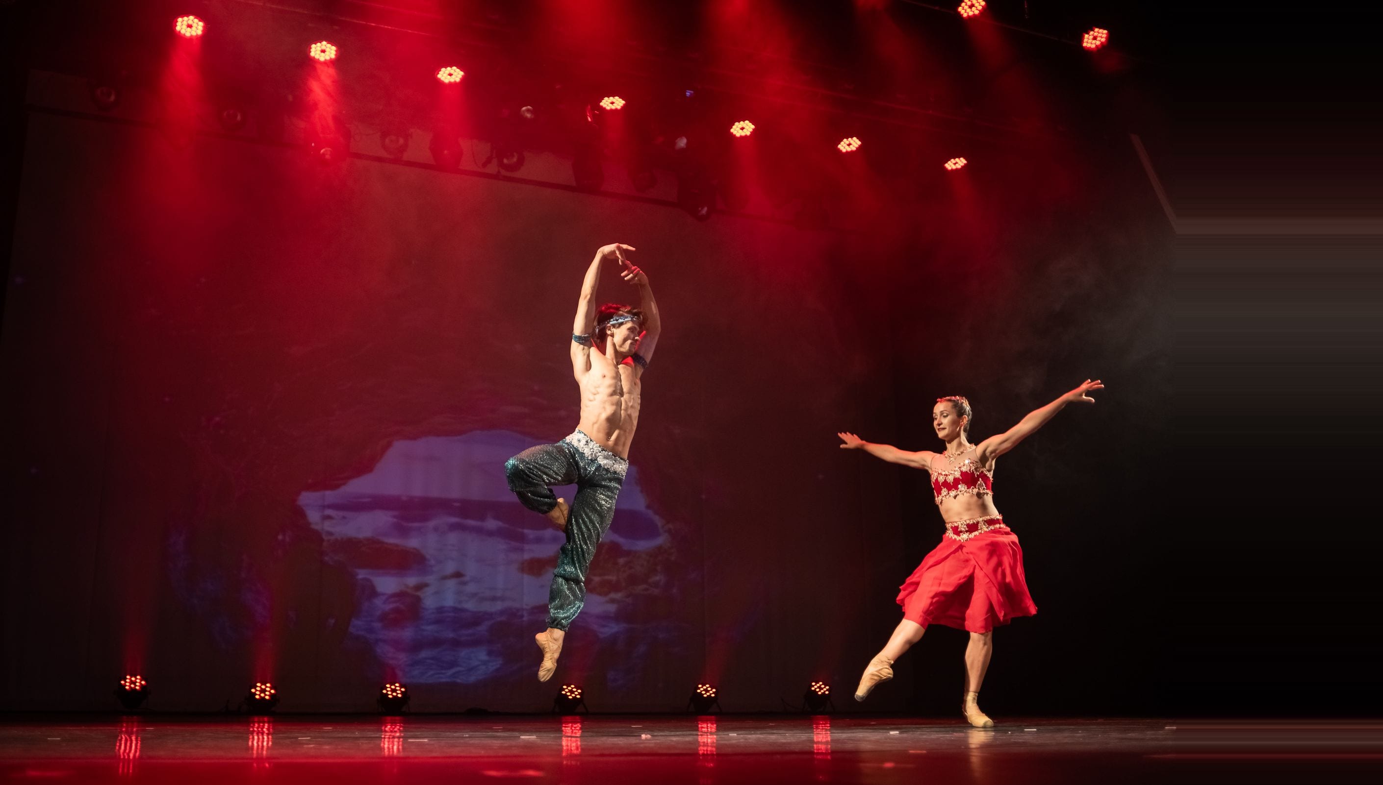 Bailarinas de amarelo no palco, ajoelhadas, erguendo arcos prateados